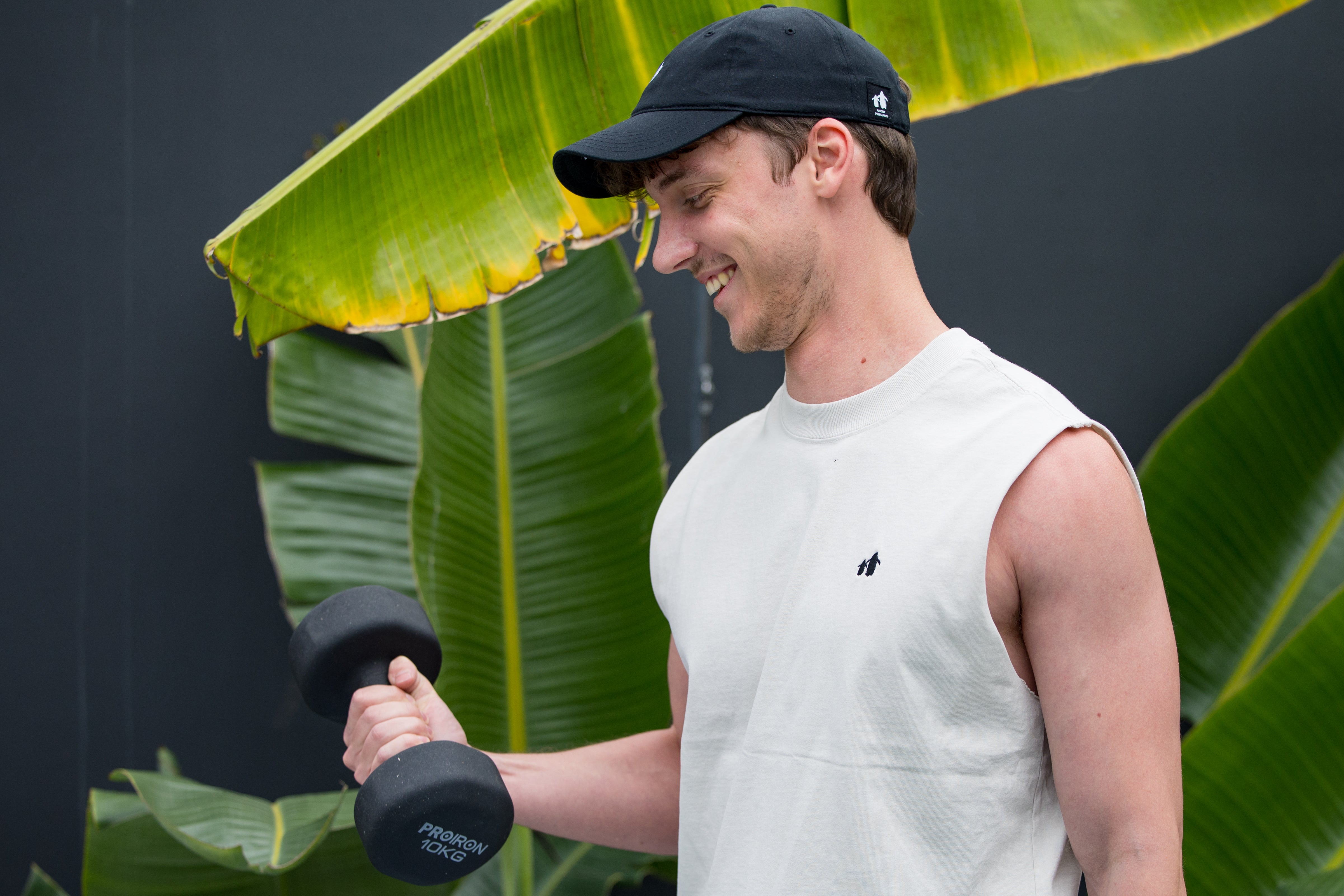 Man exercising with a dumbbell outdoors, surrounded by large green leaves. | Angry Penguins