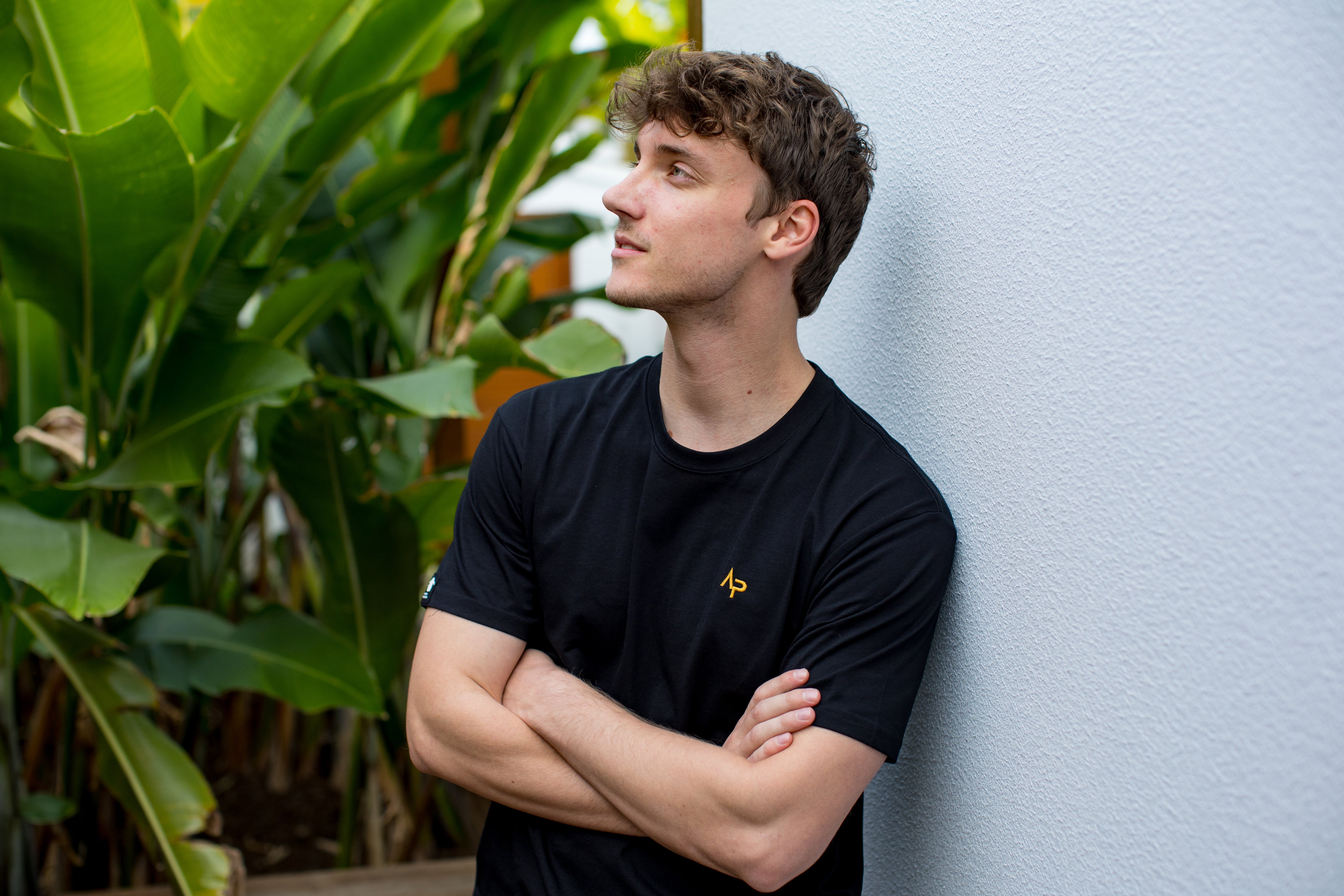 Man wearing a black t-shirt with a logo, standing against a light blue wall with greenery. | Angry Penguins