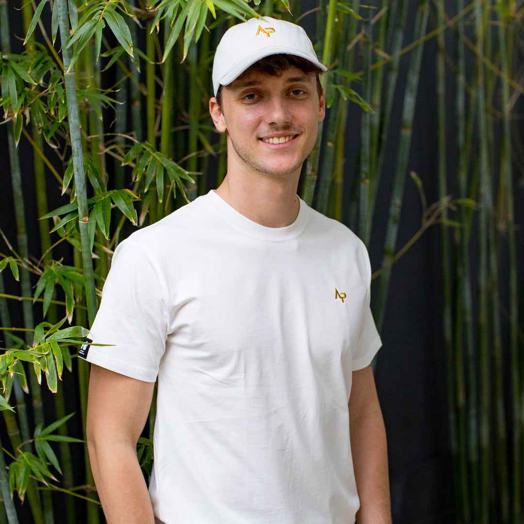 Person wearing a natural AP t-shirt and cap standing in front of bamboo plants | Angry Penguins