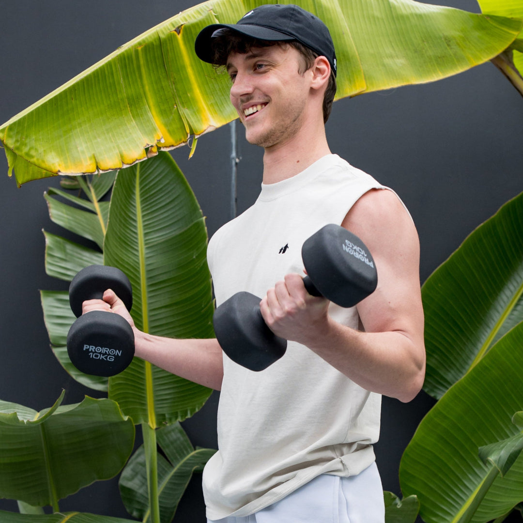 Man exercising with dumbbells in front of a dark wall and plants