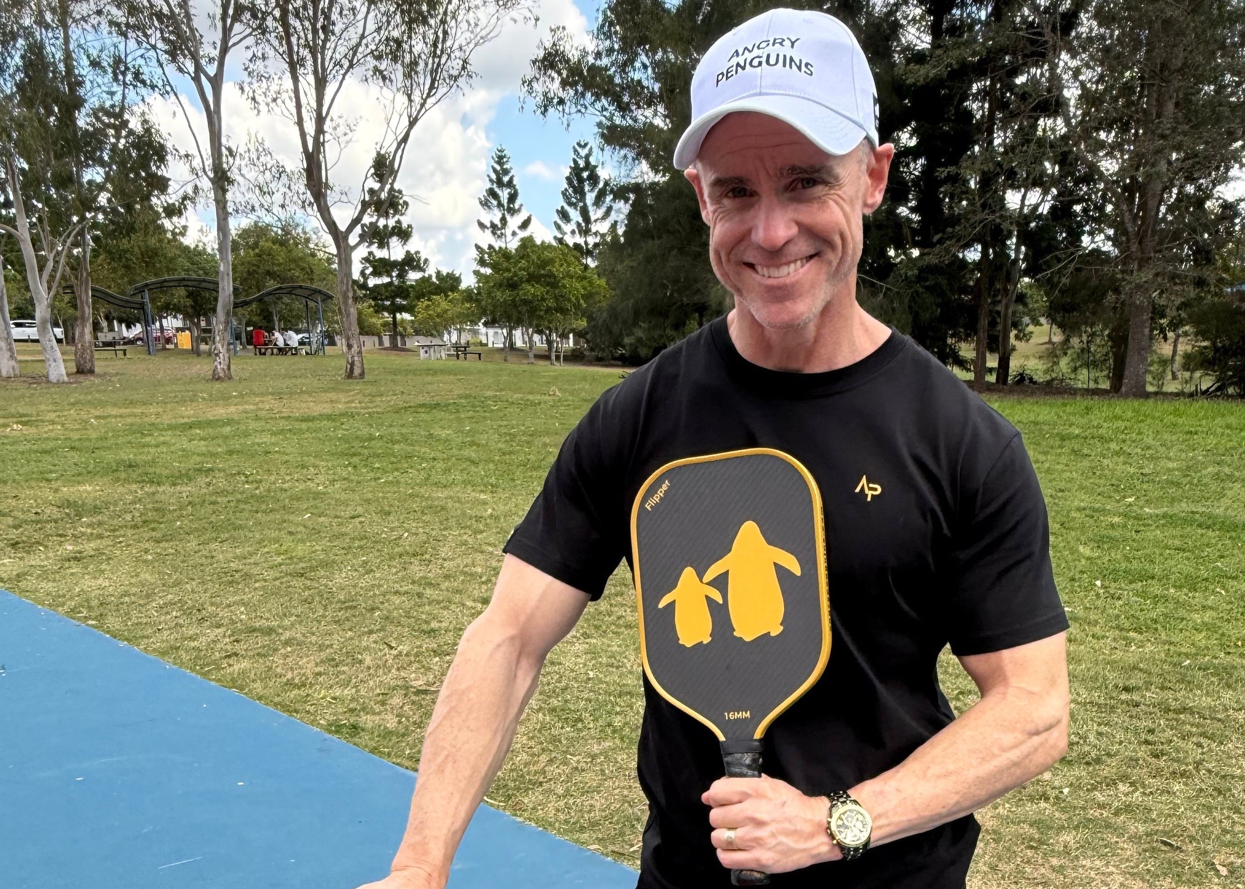 Man holding a pickleball paddle with a park in the background | Angry Penguins